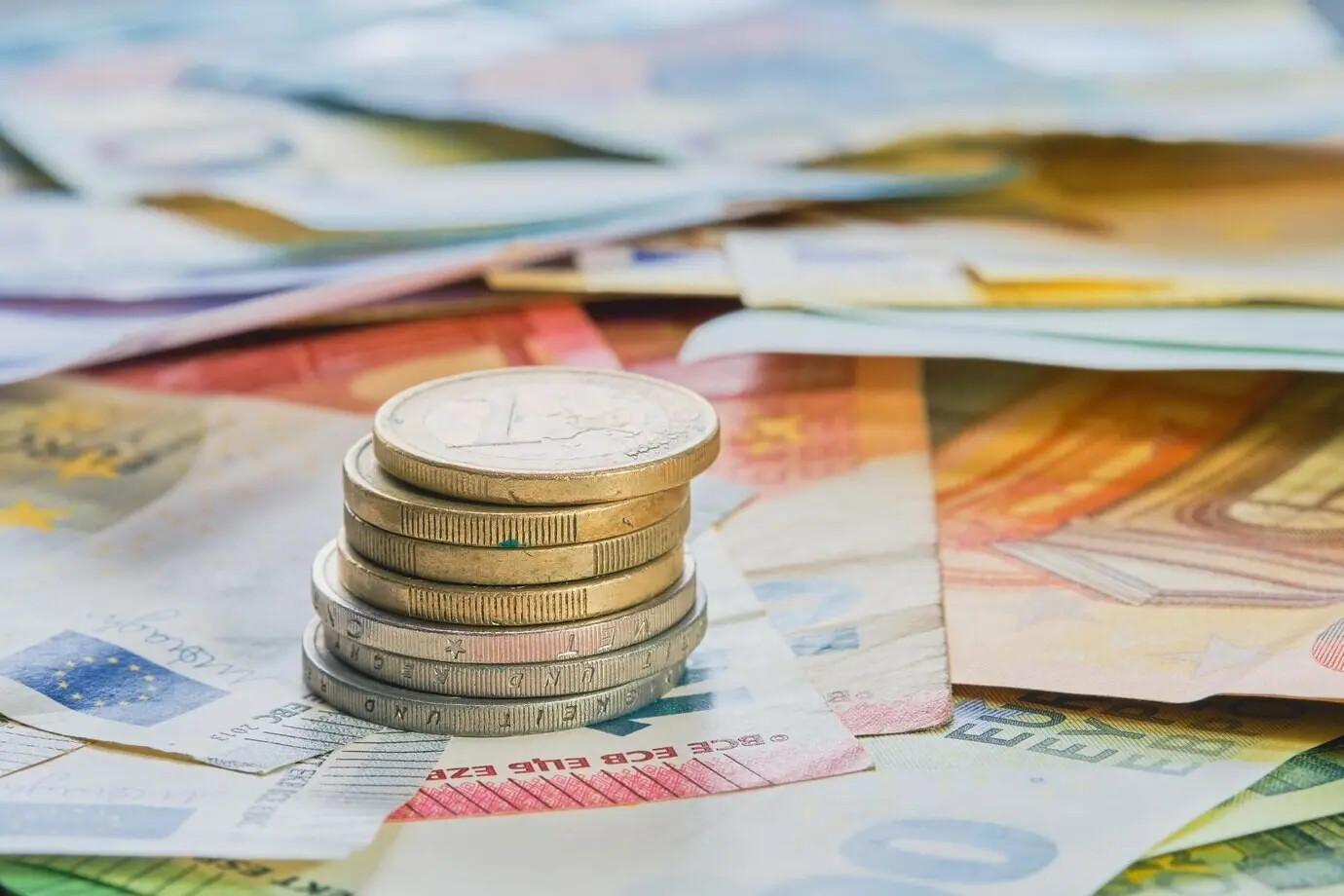 Eurové peníze: euromince naskládané na sebe v různých polohách na pozadí eurových bankovek. Koncept podnikových financí, úvodní obrazovka byznysových zpráv, mockup banneru.